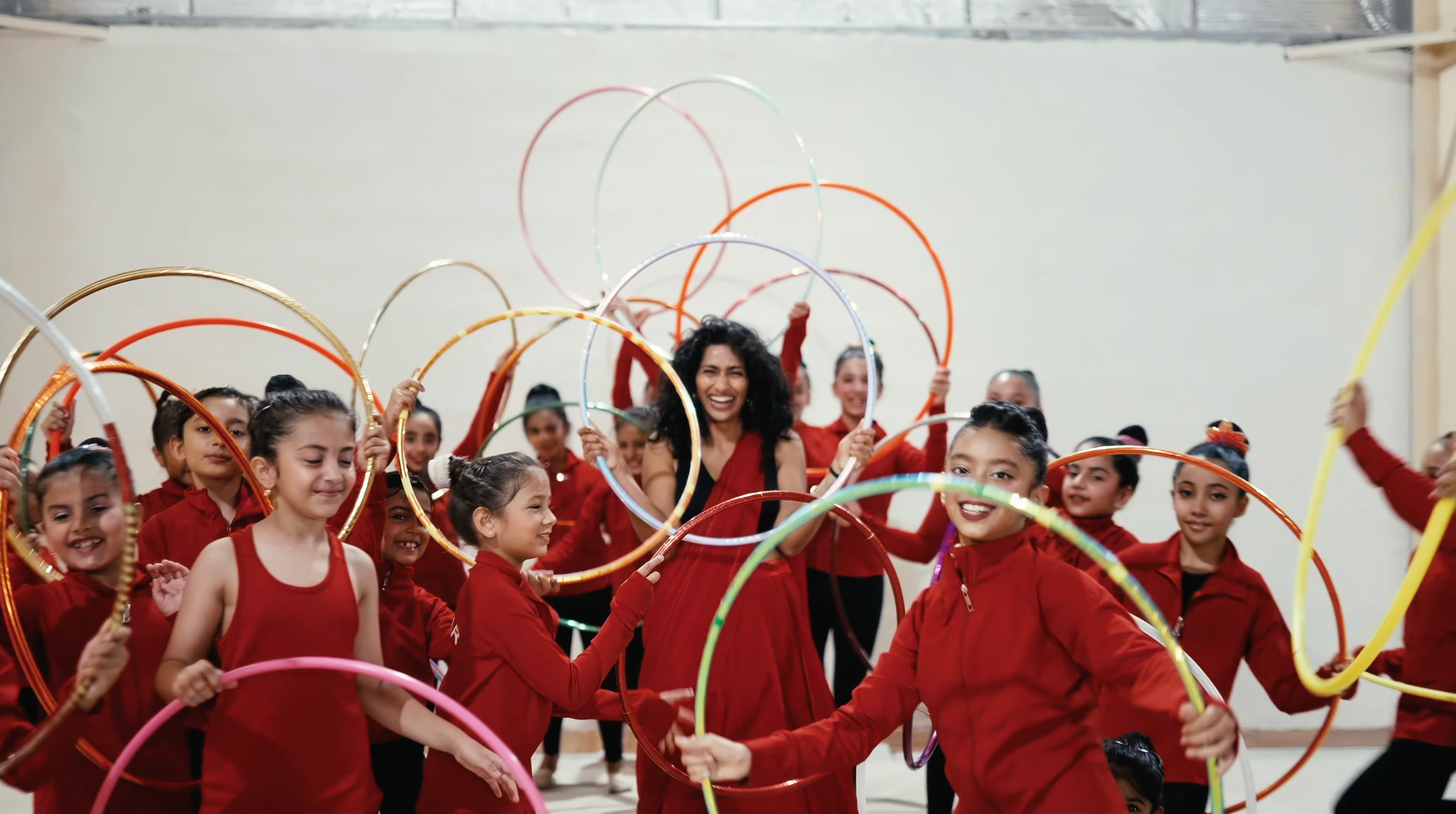 Eshna & Hoop Flo kids in red outfits with hula hoops in a dance studio.