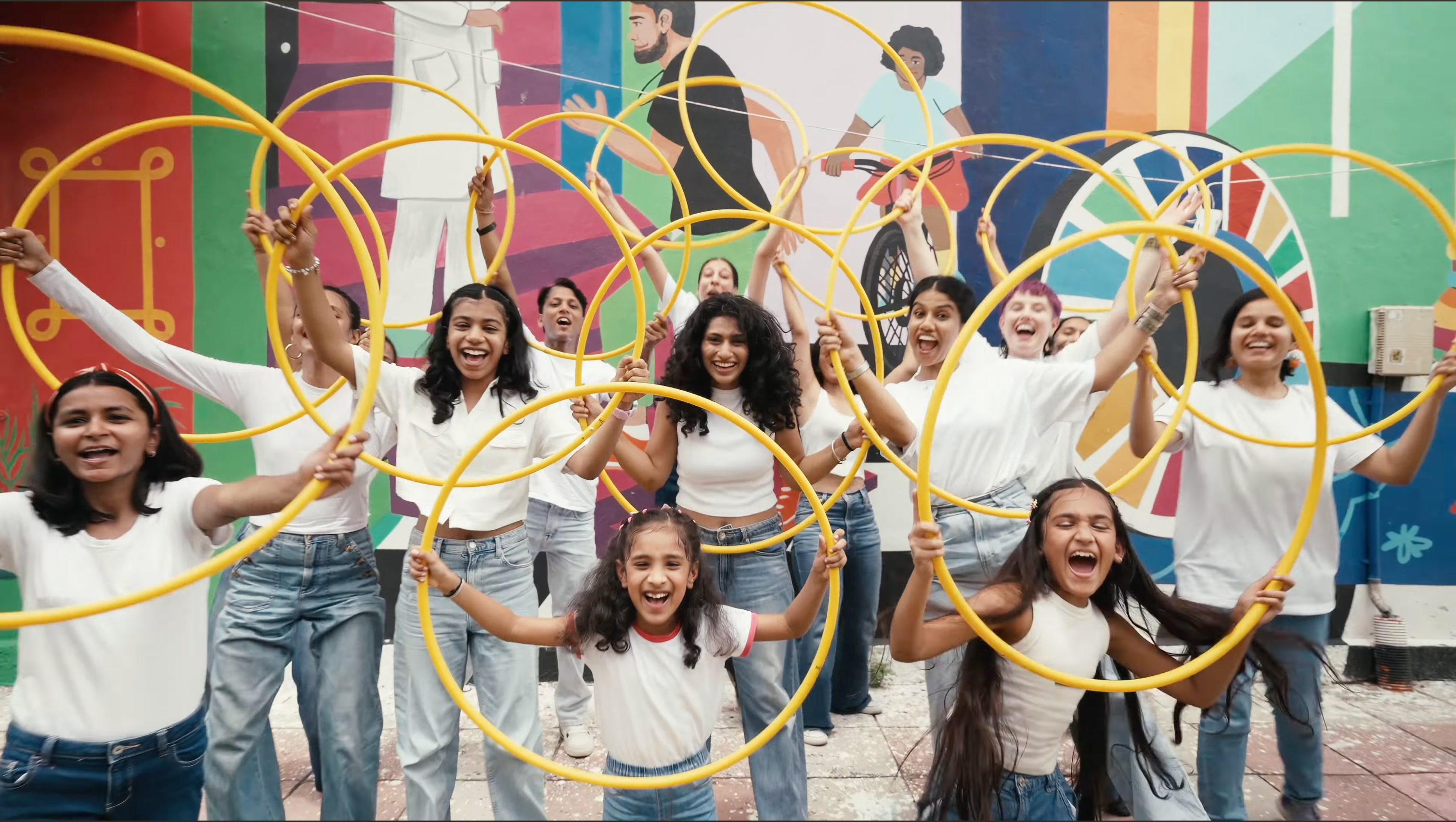 Eshna & friends with yellow hula hoops in front of a colorful mural. Sapphire.